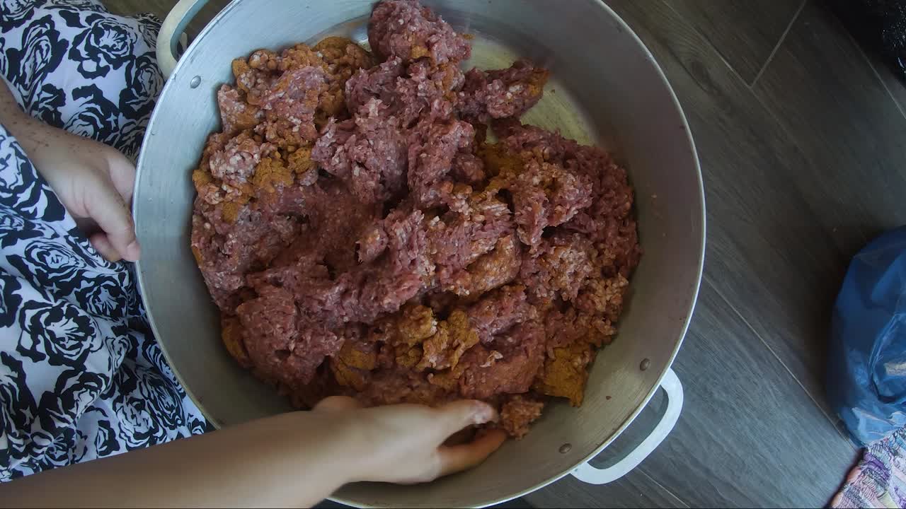 manos femeninas adultas amasando carne picada dentro de una olla grande