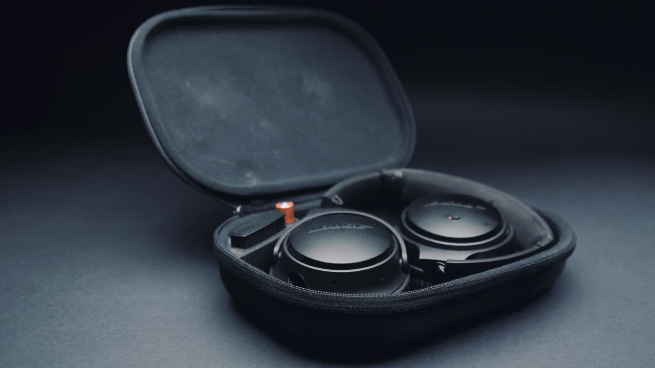 A product shot of black headphones on a black background, In a box. Camera movement  from right to left.