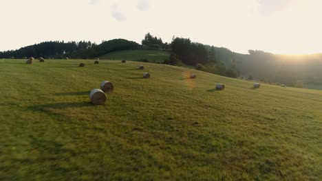 Fardos-De-Heno-Redondos-Dispersos-En-Prado-Verde-En-La-Granja,-Vuelo-De-Drones-Al-Atardecer