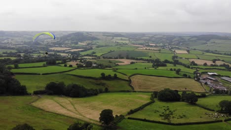 Aerial-shot-of-a-Paraglider-flying-over-the-Devon-Countryside-in-England