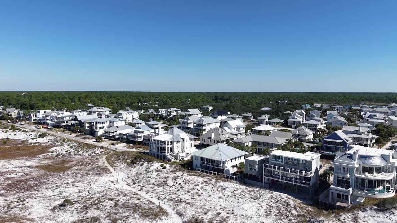 Drone fly from white sandy beach and turquoise ocean towards modern luxury coastal houses, 30A, Florida, USA