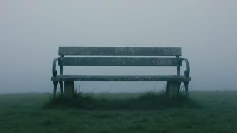 a tranquil park setting in the early morning showcases a lonely bench surrounded by thick fog. the serene atmosphere invites reflection and calmness amidst nature's beauty.