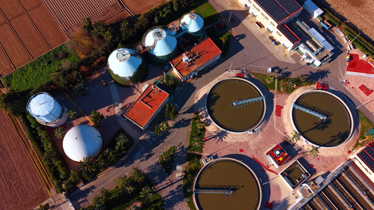 Aerial top view of circular tanks at water treatment plant. Top down view of industrial facility with circular water sedimentation tanks and silos in bright sunlight