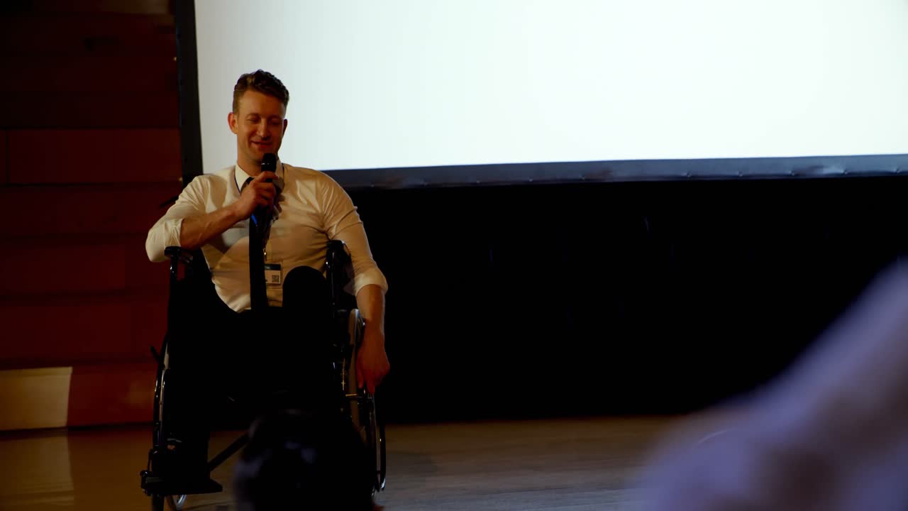젊은 백인 장애인 사업가가 4k 강당에서 비즈니스 세미나에서 연설하고 있습니다.