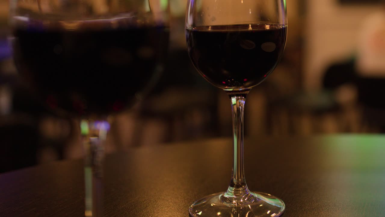 Hand places banknote beside glass of red wine on dimly lit bar table