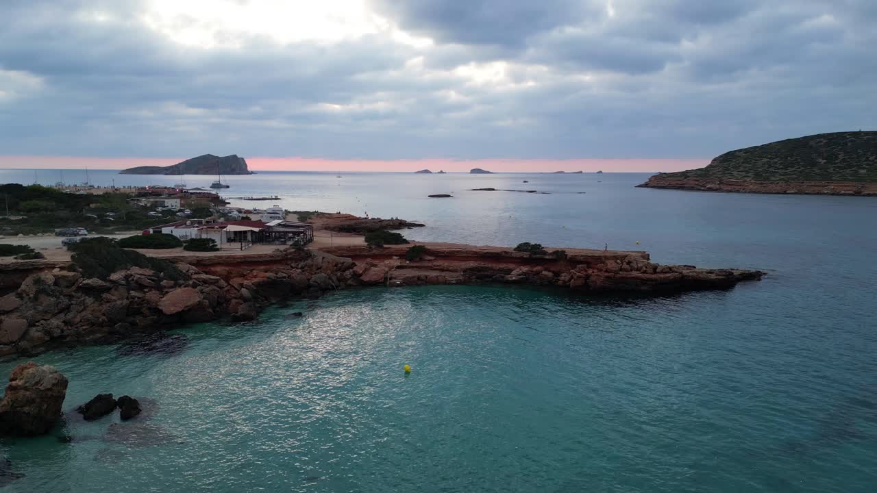 Sulava ilmakuva lento joogatyttö puuasennossa auringonlaskun aikaan, kallio, ranta, saari, Ibiza, Espanja, laskeutuva drone.