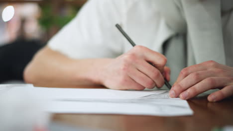 close up shot of hands leaning on wooden table while sketching intricate pencil outlines on white paper capturing artistic process and focused craftsmanship showing delicate fluid motion precision