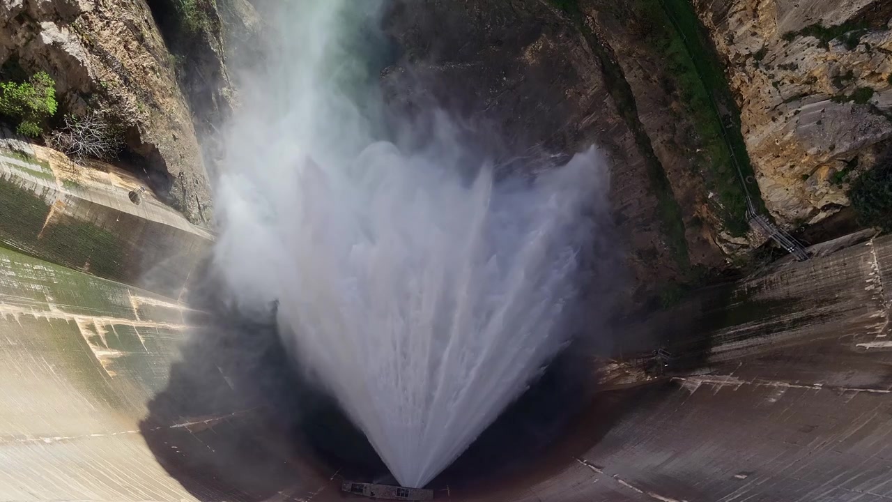 Scarico d'acqua da una diga all'interno di un canyon di montagna. Acqua pressurizzata che esce dalla diga. Valvola Howell Bunger in funzione. Vista aerea dall'alto.