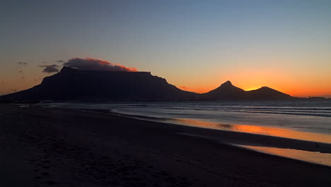 Atemberaubende-Kapstadt-Tafelberg-Strand-Silhouette-Landschaft,-Tieforangefarbener-Abend,-Später-Sonnenuntergang,-Südafrika,-Ebbe,-Unglaubliche-Küstenlinie,-Ende-Des-Tages,-Wellen,-Krachender-Frieden,-Zeitlupe,-Schwenk-Nach-Links