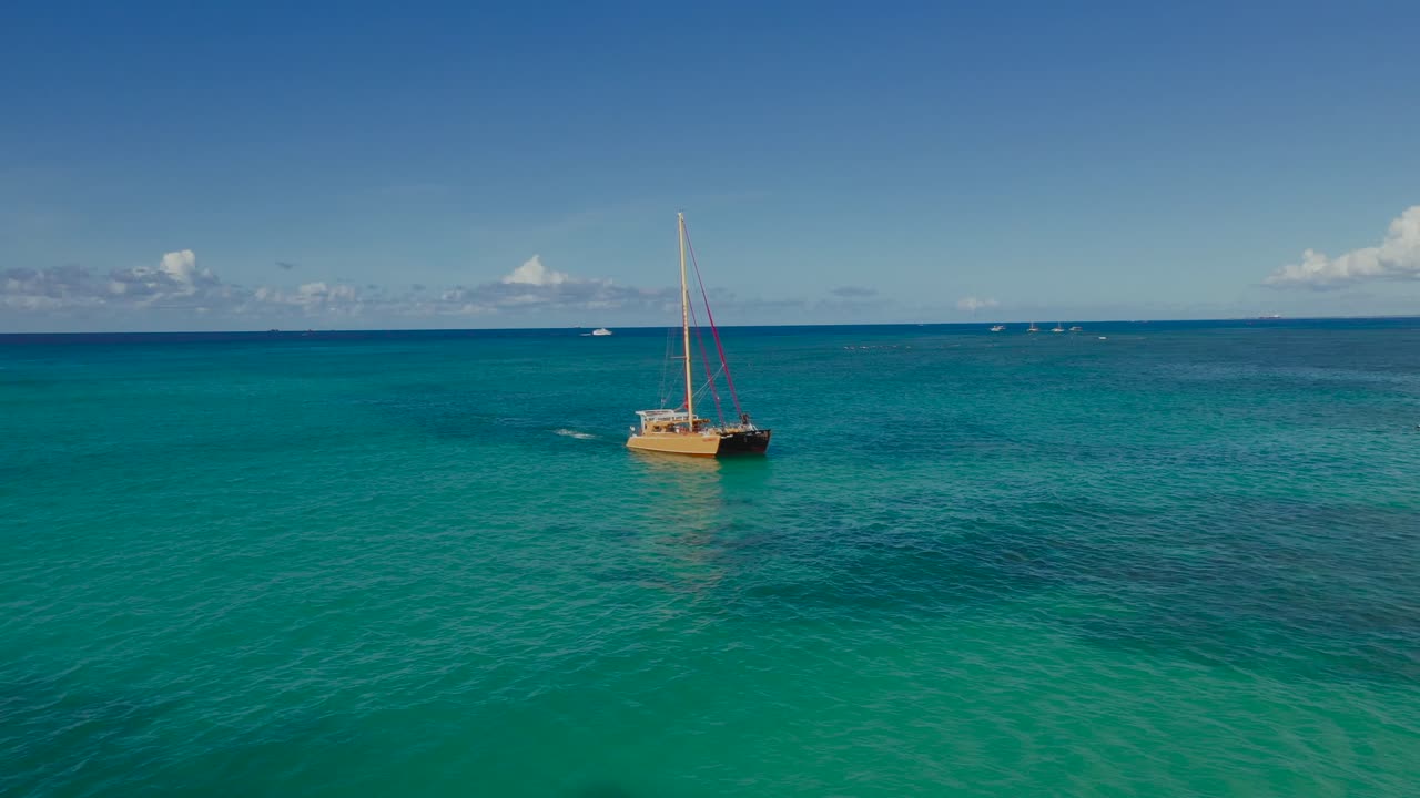 Drone video of a wooden sailboat gliding across open turquoise sea near Waikiki Beach, Oahu, Hawaii. A tranquil aerial scene capturing island adventure, ocean clarity, and timeless maritime charm