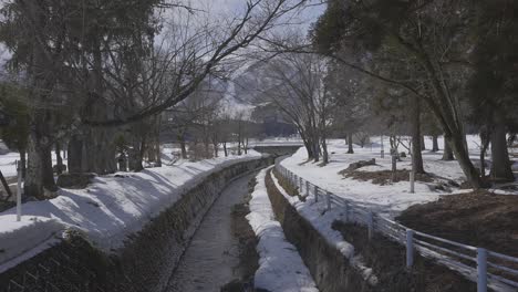 evocando una sensación de paz, la cámara revela la pintoresca escena de un arroyo de agua que se teje pacíficamente su camino a través de la ciudad cubierta de nieve de hakuba durante el día