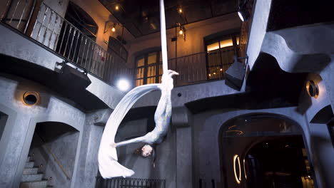 female aerialist performing a headlong drop on silks in a club venue