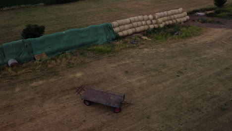 vuelo ascendente frente a un remolque abandonado en medio de un campo y pacas en el fondo