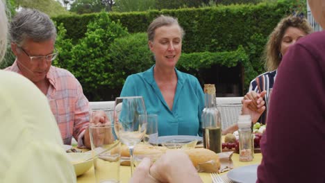 Animation-of-happy-diverse-female-and-male-senior-friends-having-lunch-in-garden,-praying