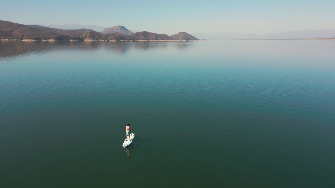 Pemandangan Udara Seorang Pria Mendayung Paddleboard di Danau yang Tenang dengan Pegunungan