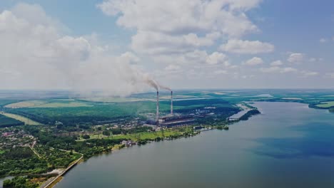aerial view of plant on the bank of the river in summer. view from above on natural background of beautiful river and factory with smoke from pipes. slow motion. camera moves up.