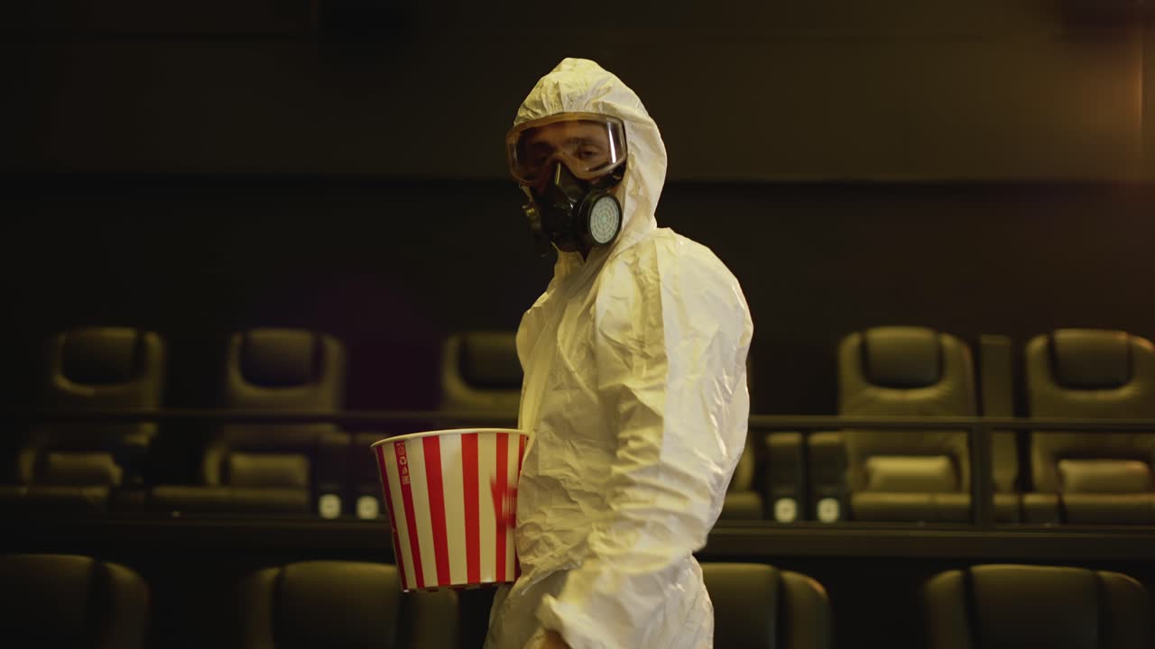 un hombre con traje de protección blanco y respirador vino solo al cine con un cubo de palomitas de maíz