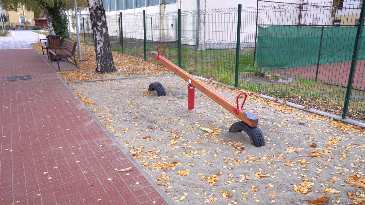 Empty Seesaw on an Autumn Playground with Falling Leaves