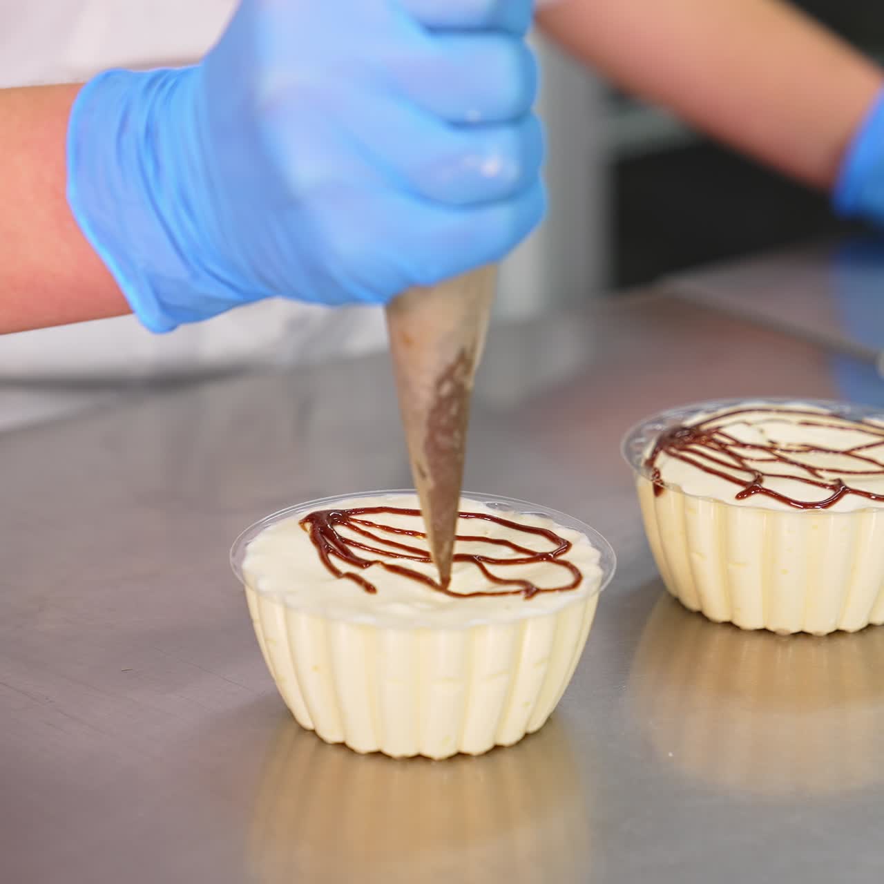White creamy desserts being decorated with caramel. Gloved hand squeezes liquid caramel from pastry bag on the cups with sweets. Close up