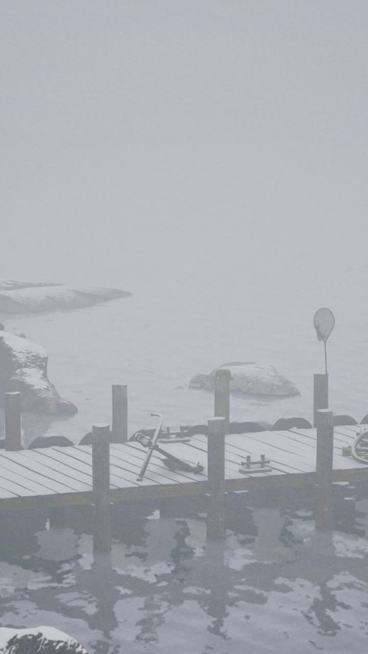 Misty winter harbor with a snowy dock and rocky shores surrounded by fog