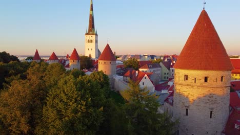 tallinn’s medieval towers and spire rise above green trees in golden evening sunlight