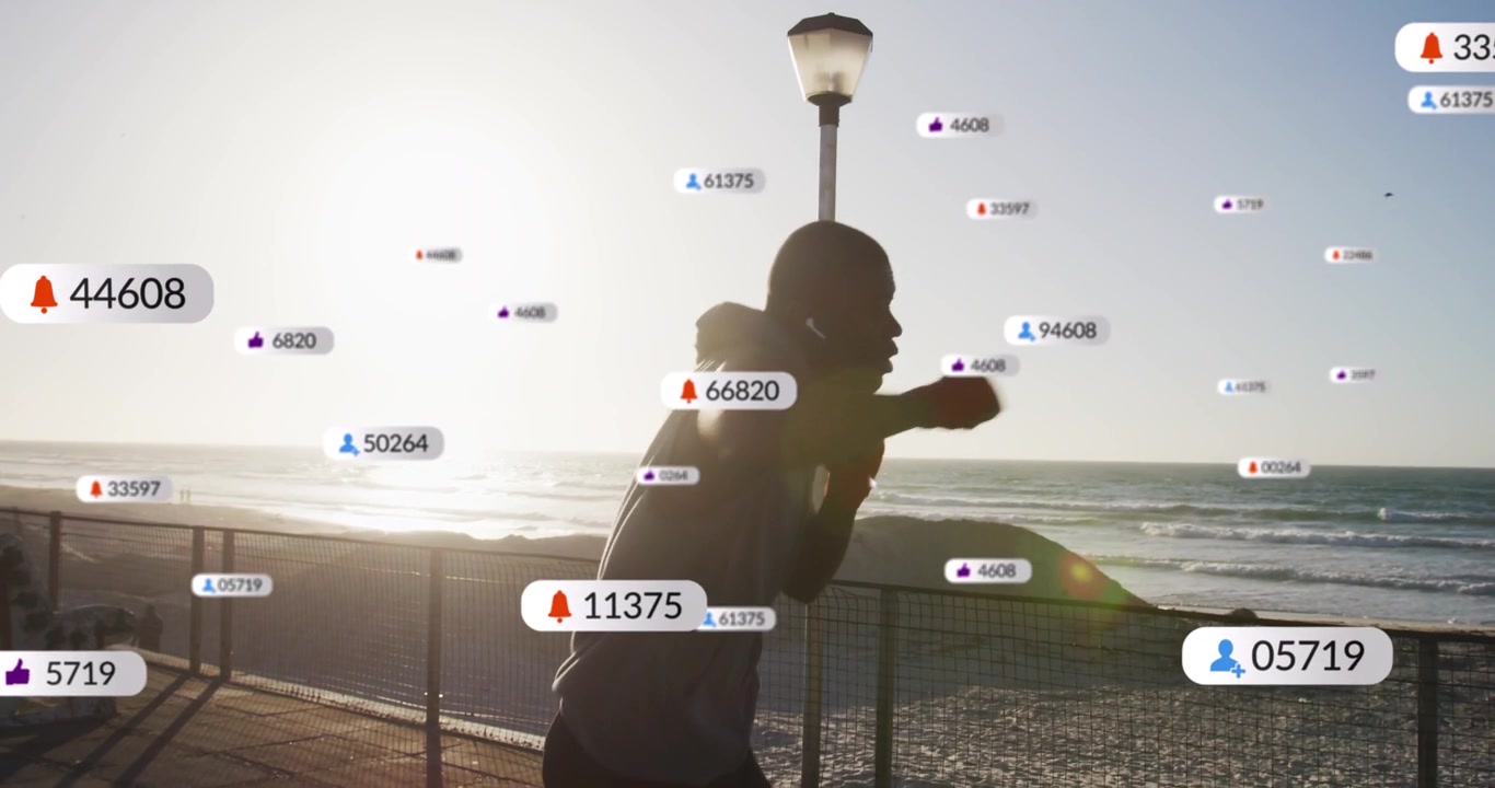 Mid adult man in dark hoodie training, throwing jabs along seaside railing, UI badges accumulating