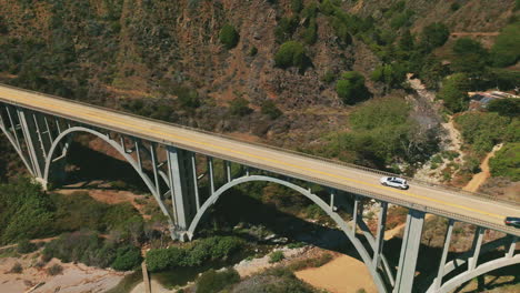 beautiful metal arched bridge in the mountains of california shore. little sandy beach among the rocks of pacific coastline. sunny day backdrop.