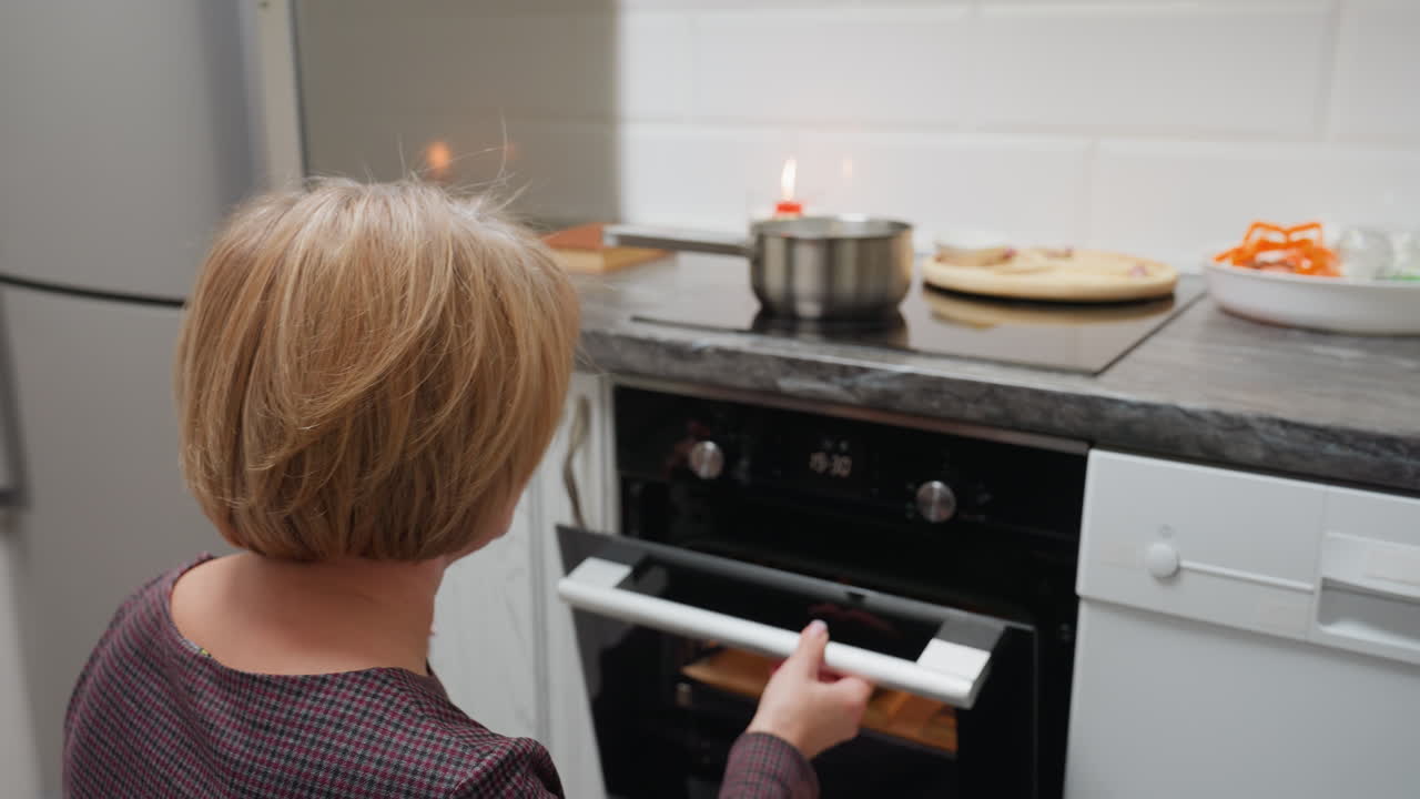 Donna che osserva i biscotti nel forno mentre lo richiude, concentrandosi sul processo di cottura, cucina ben illuminata, guarda i biscotti con attenzione, preparando biscotti fatti in casa da cuocere