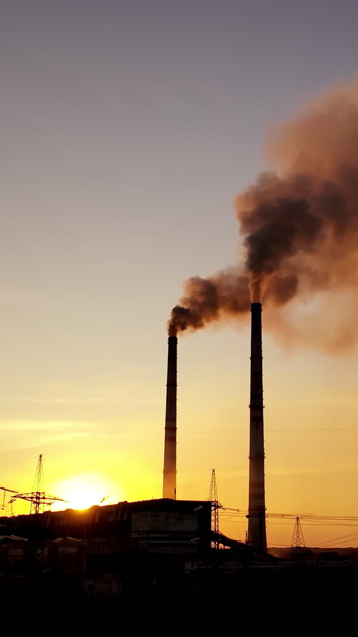 Evening background of industrial factory. Dirty smoke goes from pipes at sunset. Metallurgical plant with smoke on the evening sky. Vertical video