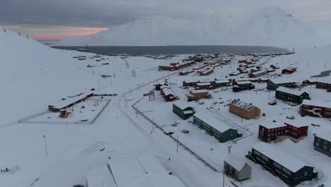 drone view in svalbard flying over longyearbyen town showing houses in a snowy area with a fjord and mountain in norway