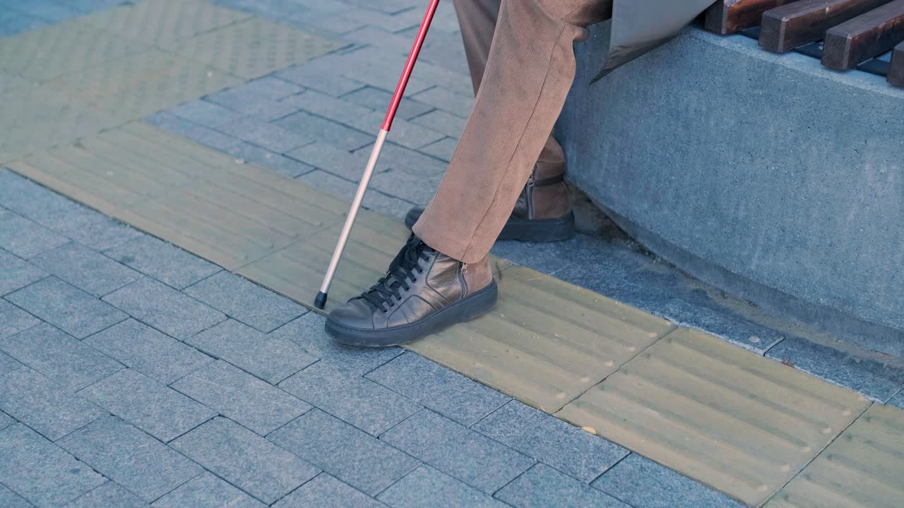 Blind person using white cane on straight tactile tiles to navigate road