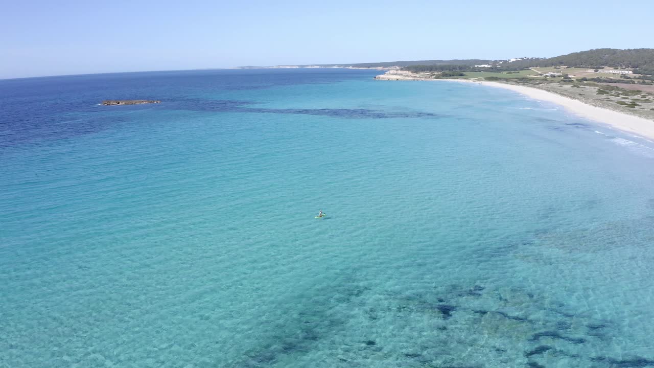 Drone che riprende con panoramica un praticante di stand up paddle a Minorca, Spagna, in una giornata estiva.