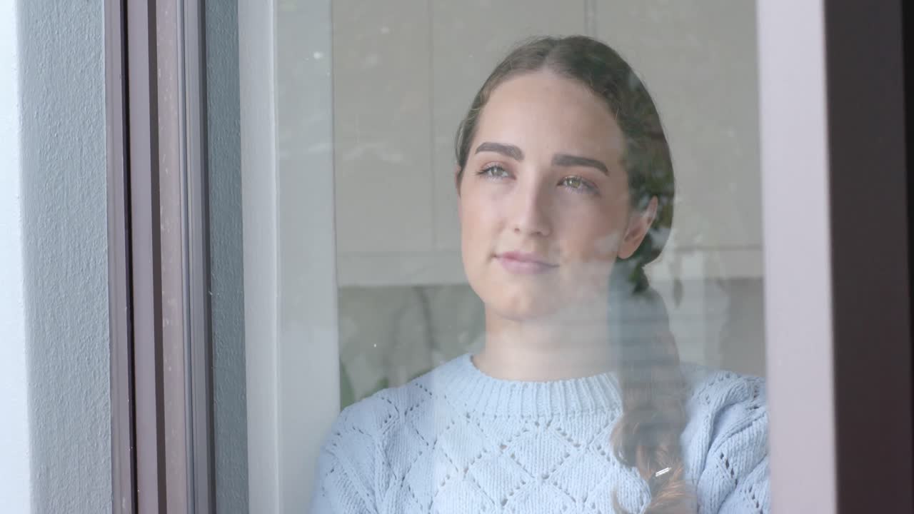 Thoughtful caucasian woman smiling and looking through window in slow motion