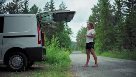 caucasian woman opens tailgate of a white van parked in a rural area