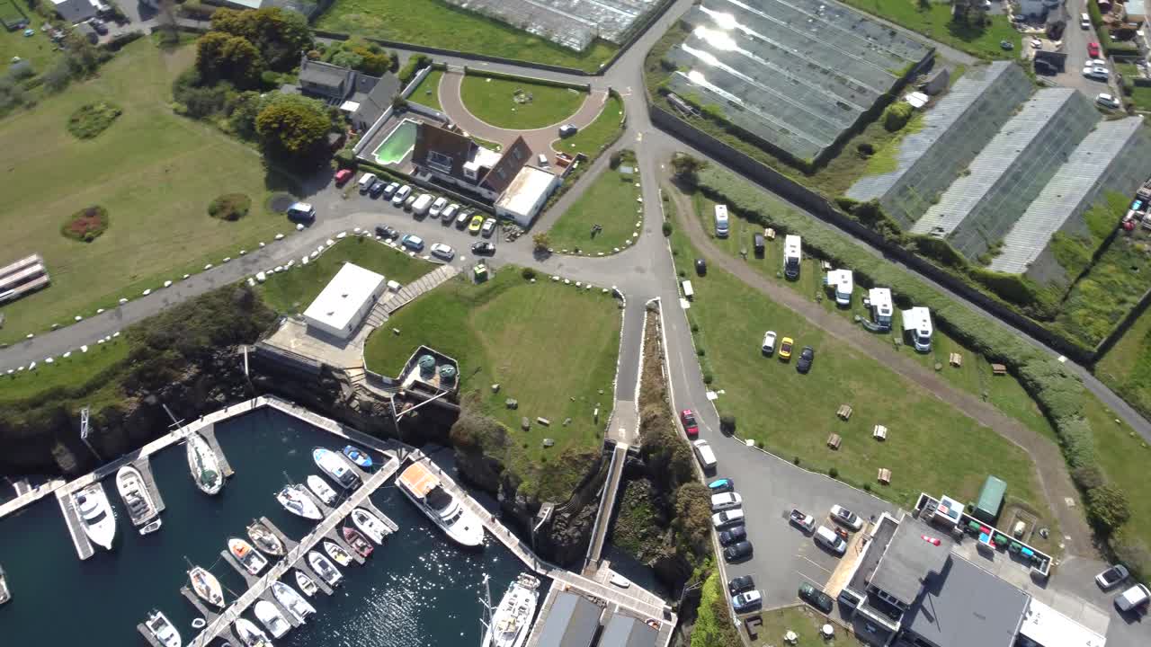 Beaucette Marina Guernsey overhead circling shot of boats berthed on pontoons in marina,boatyard,restaurant and motorhome campsite with surrounding glasshouses on bright sunny day