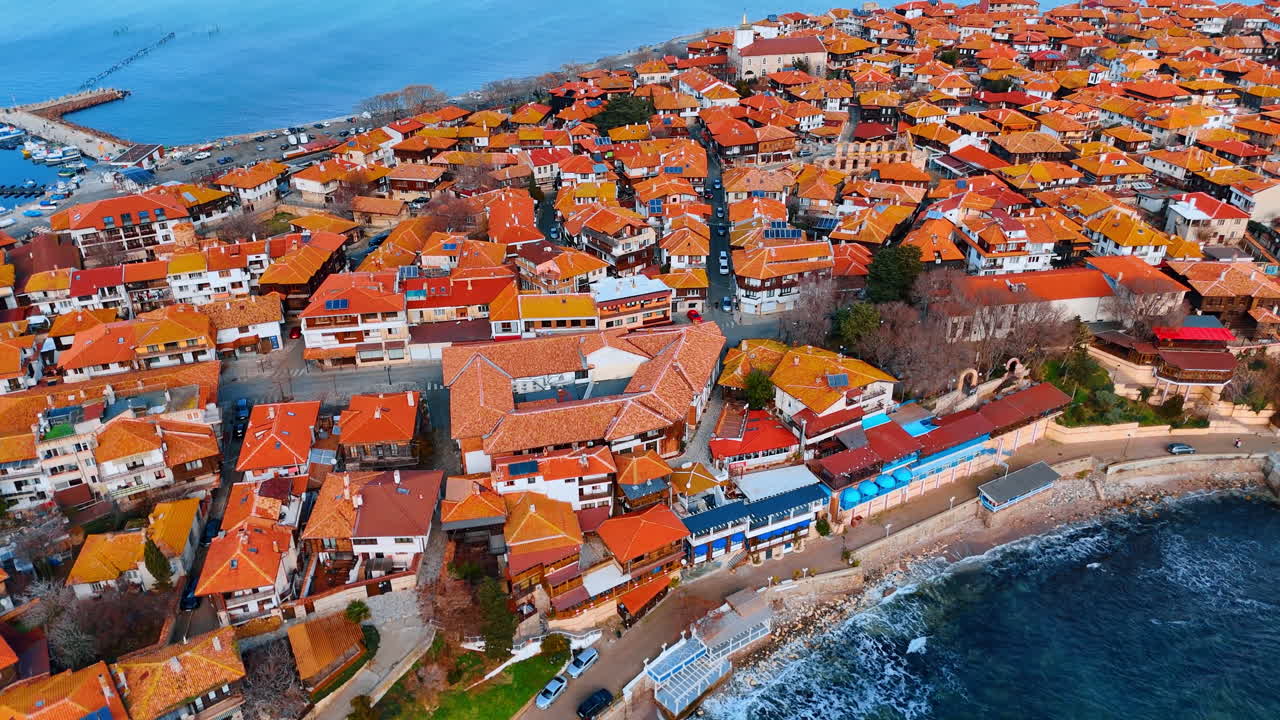 Tetti colorati su una città di mare. Case con tetti arancioni si affacciano sul mare, accanto a barche e onde tranquille, in una giornata di sole nella località.