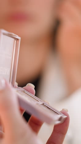 hands of woman holding eye shadow palette and applicator against blurred reflection in mirror. lady uses cosmetic product to do makeup macro
