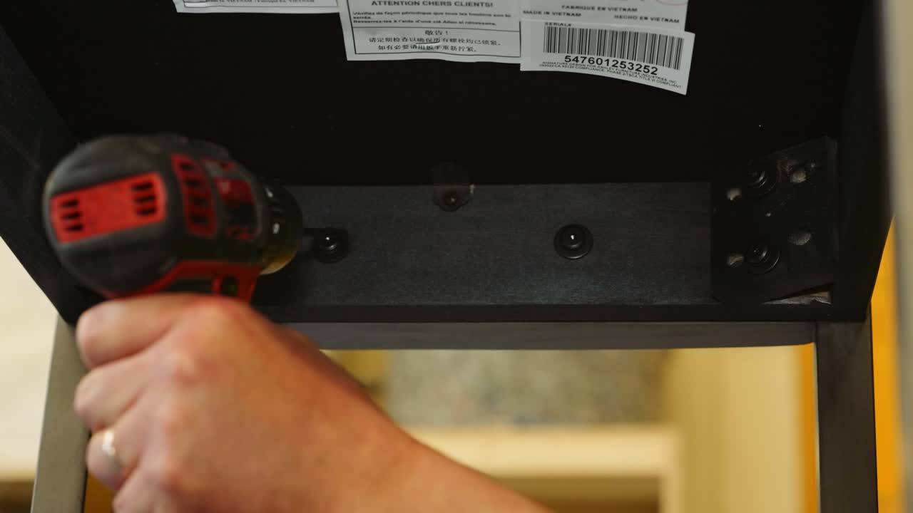 un carpintero de reparación de muebles trabaja debajo de una silla de comedor para apretar los pernos usando un taladro eléctrico y nivelar el asiento de tapicería