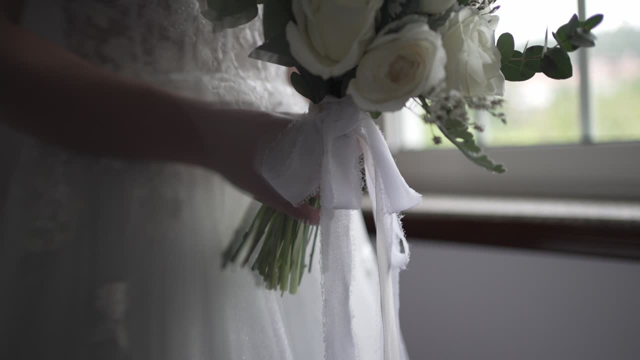 Mano che tiene un bouquet di rose bianche con nastro svolazzante vicino alla luce della finestra