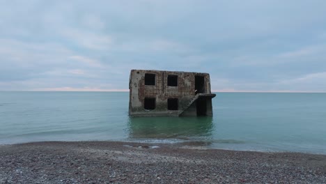 aerial view of abandoned seaside fortification building at karosta northern forts on the beach of baltic sea , waves splash, overcast day, low wide rotating drone shot