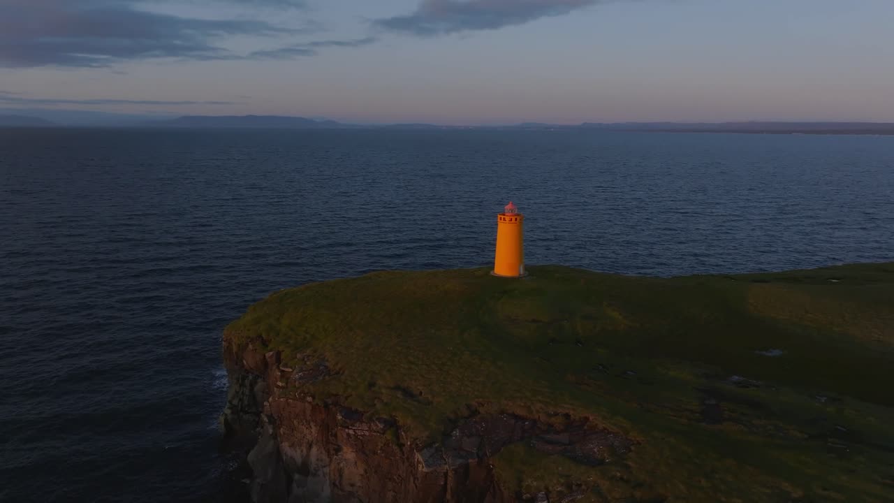 Sapuan drone sinematik mercusuar kuning Keflavik, tebing terjal, dan deburan ombak laut.