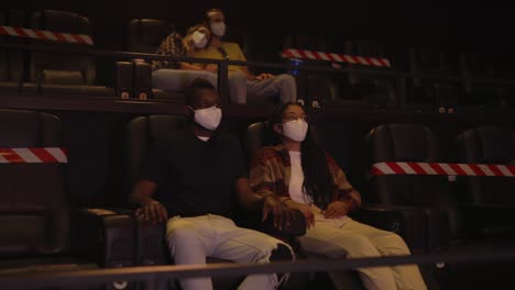 african man and woman enjoying film during pandemic, wearing white face masks