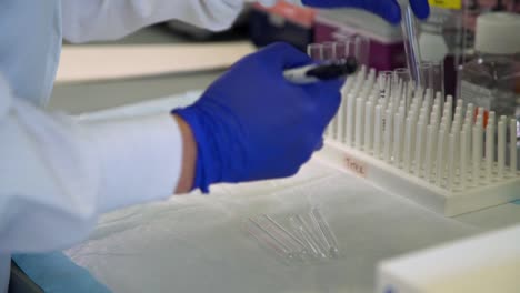 un técnico de laboratorio con una bata blanca y guantes azules etiqueta viales pequeños con un marcador negro