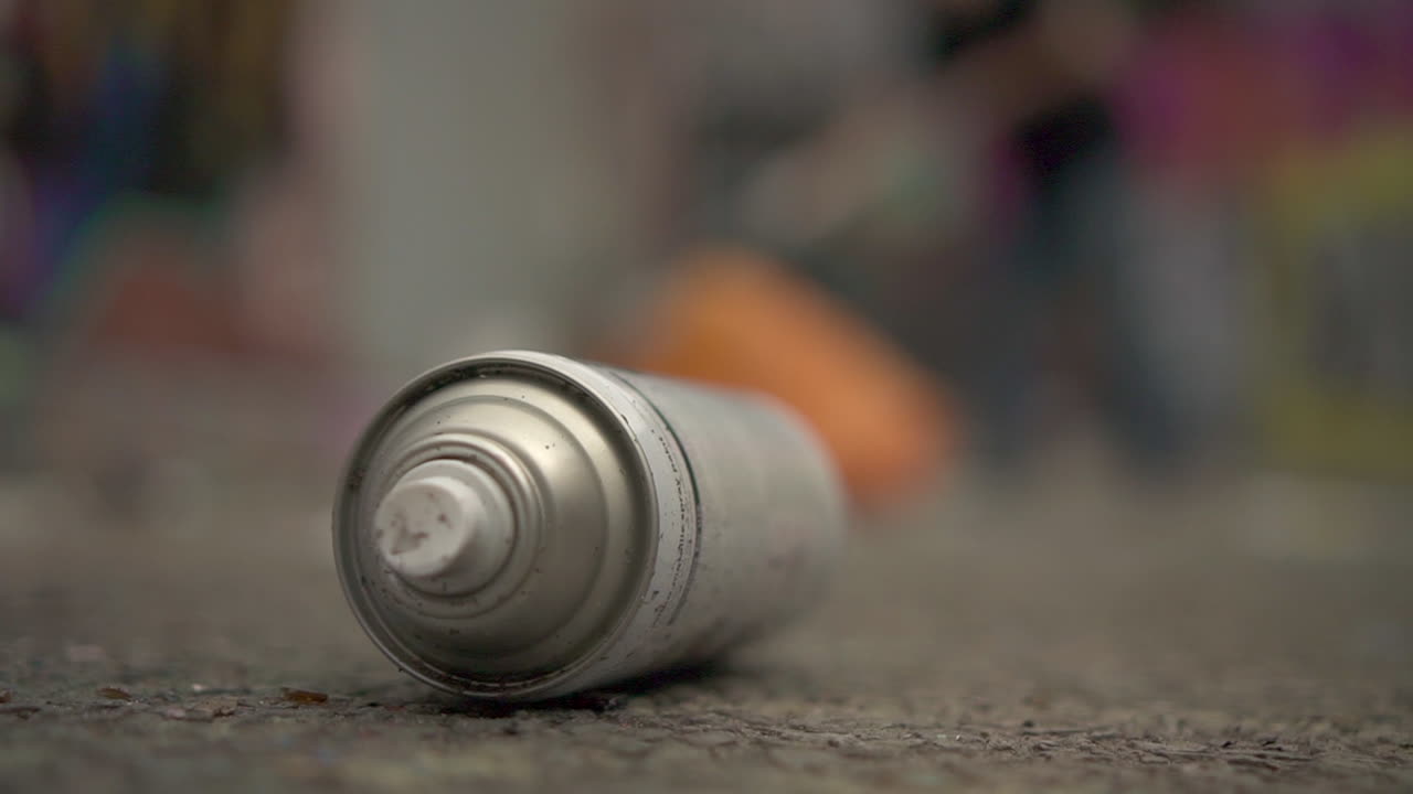 누군가가 전경에서 벽을 칠하는 동안 스프레이 페인트 병을 닫습니다.