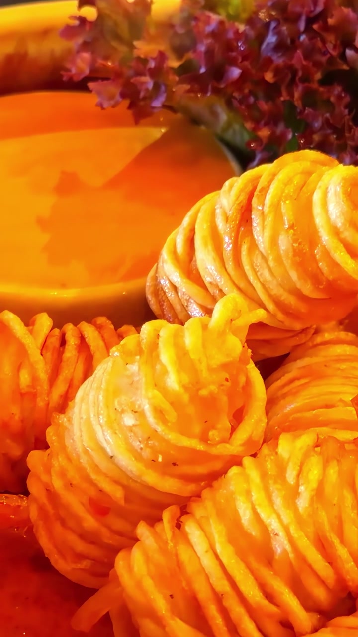 Golden crispy curly fries arranged beside a bowl of spicy dipping sauce and fresh red lettuce, offering a warm and appetizing snack moment.