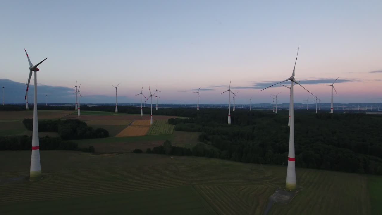 Drone aerial flying towards wind turbine farm in a large open field