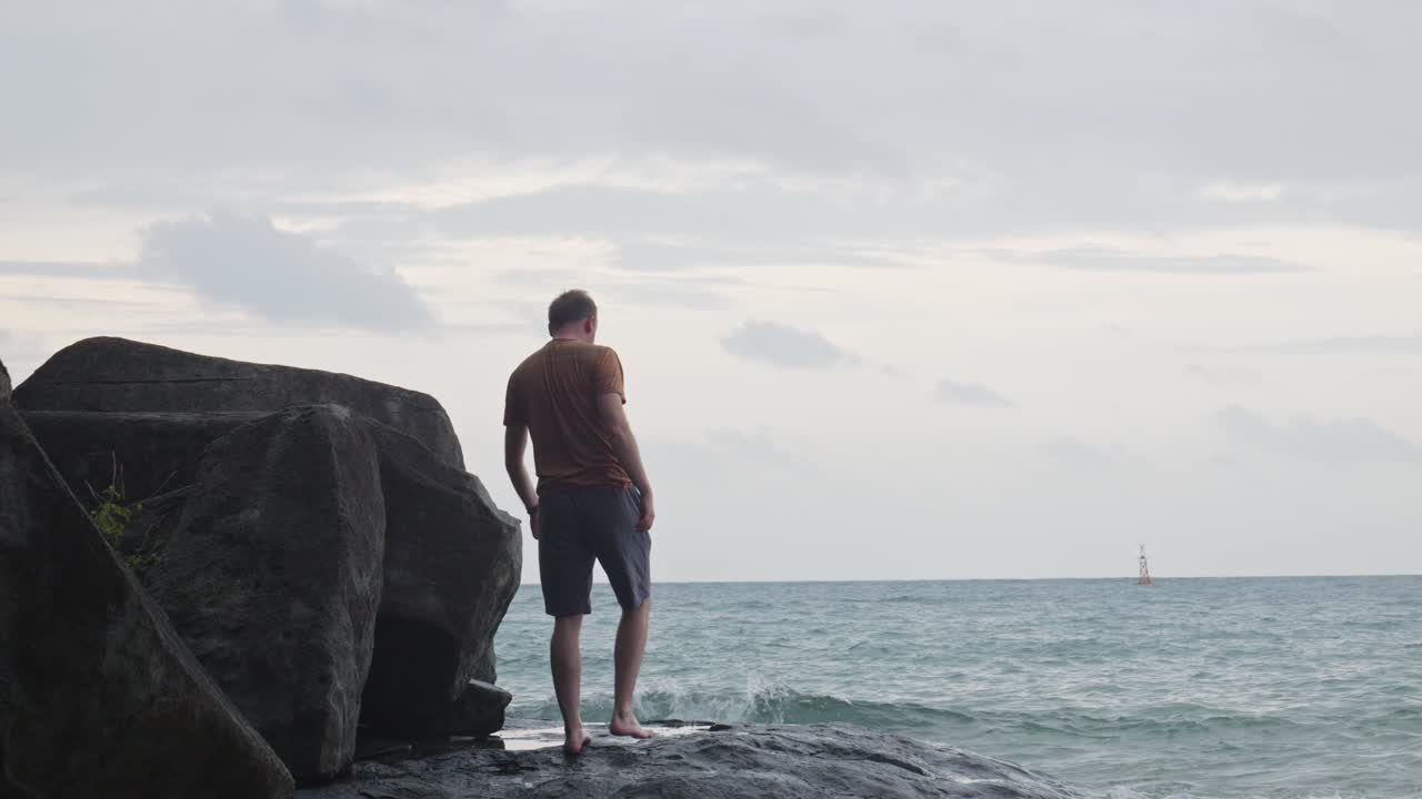 tipo caminando en la costa rocosa de la playa para admirar el océano ondulado