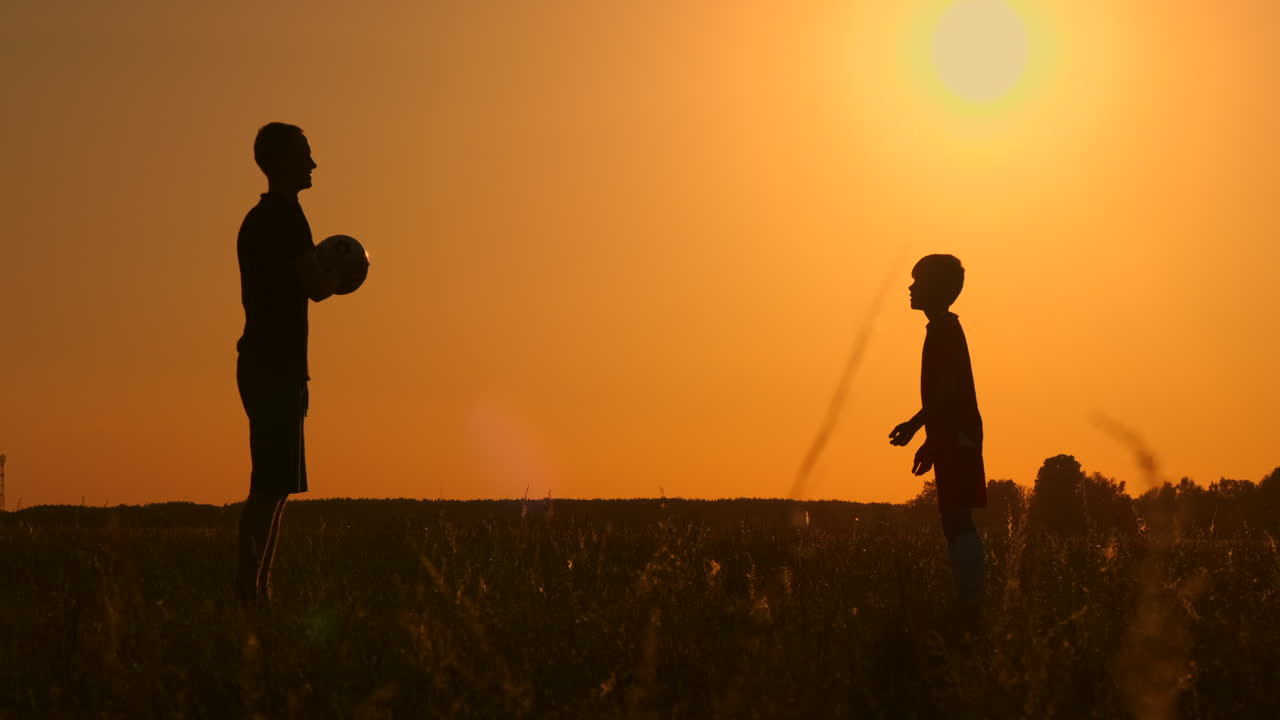 padre e figlio che giocano a calcio nel parco al tramonto, silhouette sullo sfondo di un sole brillante, riprese a rallentatore.