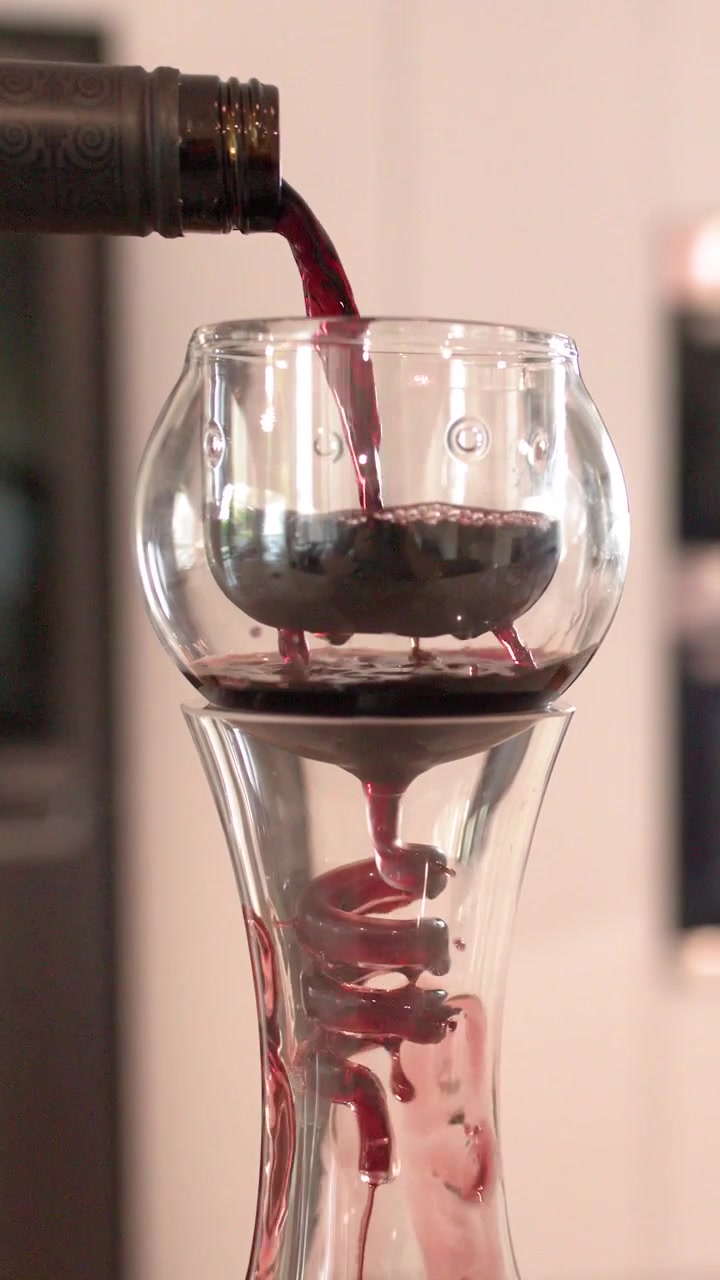 El vino tinto fluye de una botella a través de un aireador de vidrio en espiral hacia un decantador.