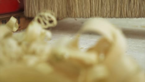 a macro shot of planned wood shavings being swept away by a carpenter in slow motion